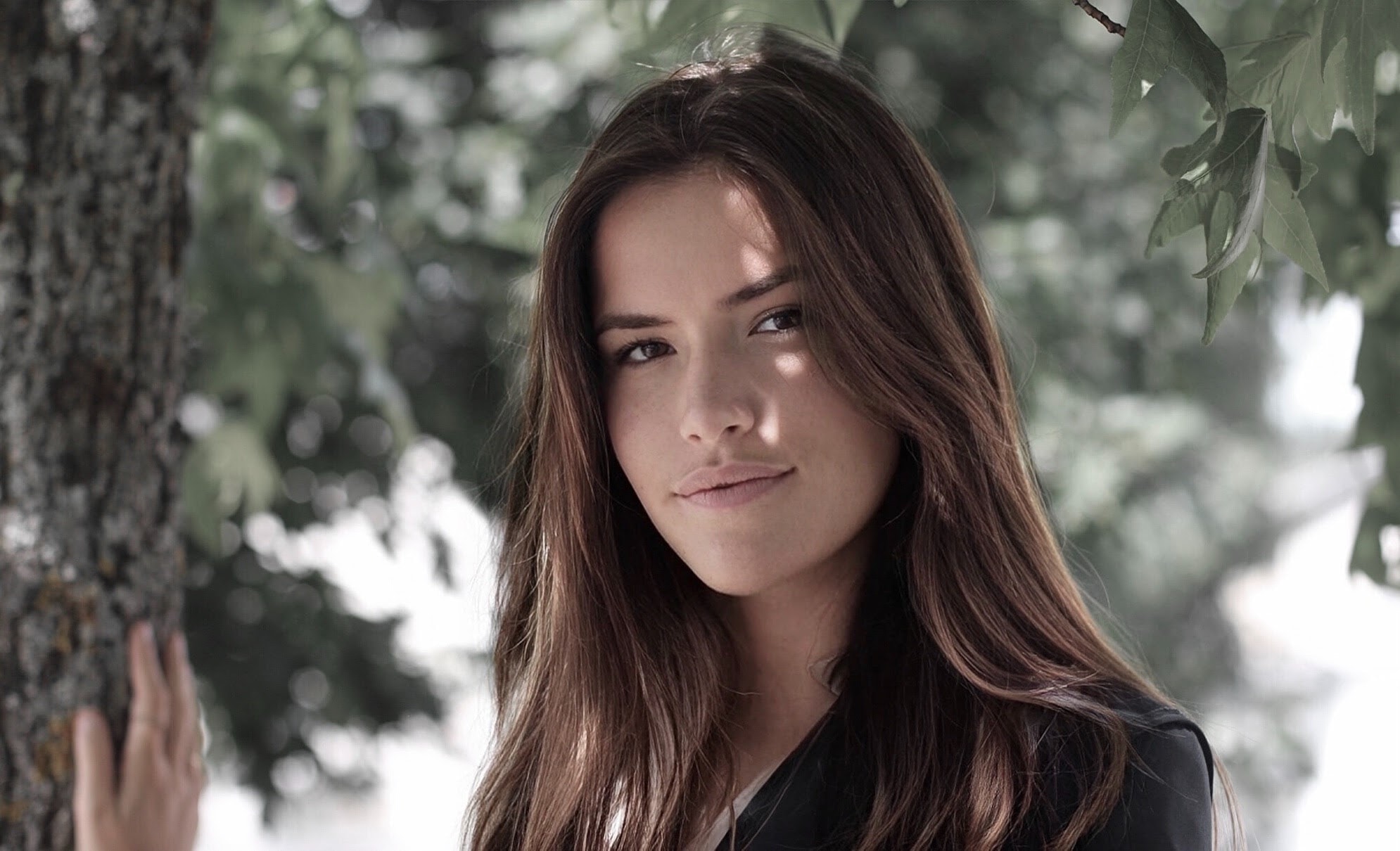 Portrait d'une jeune femme brune appuyée contre un arbre
