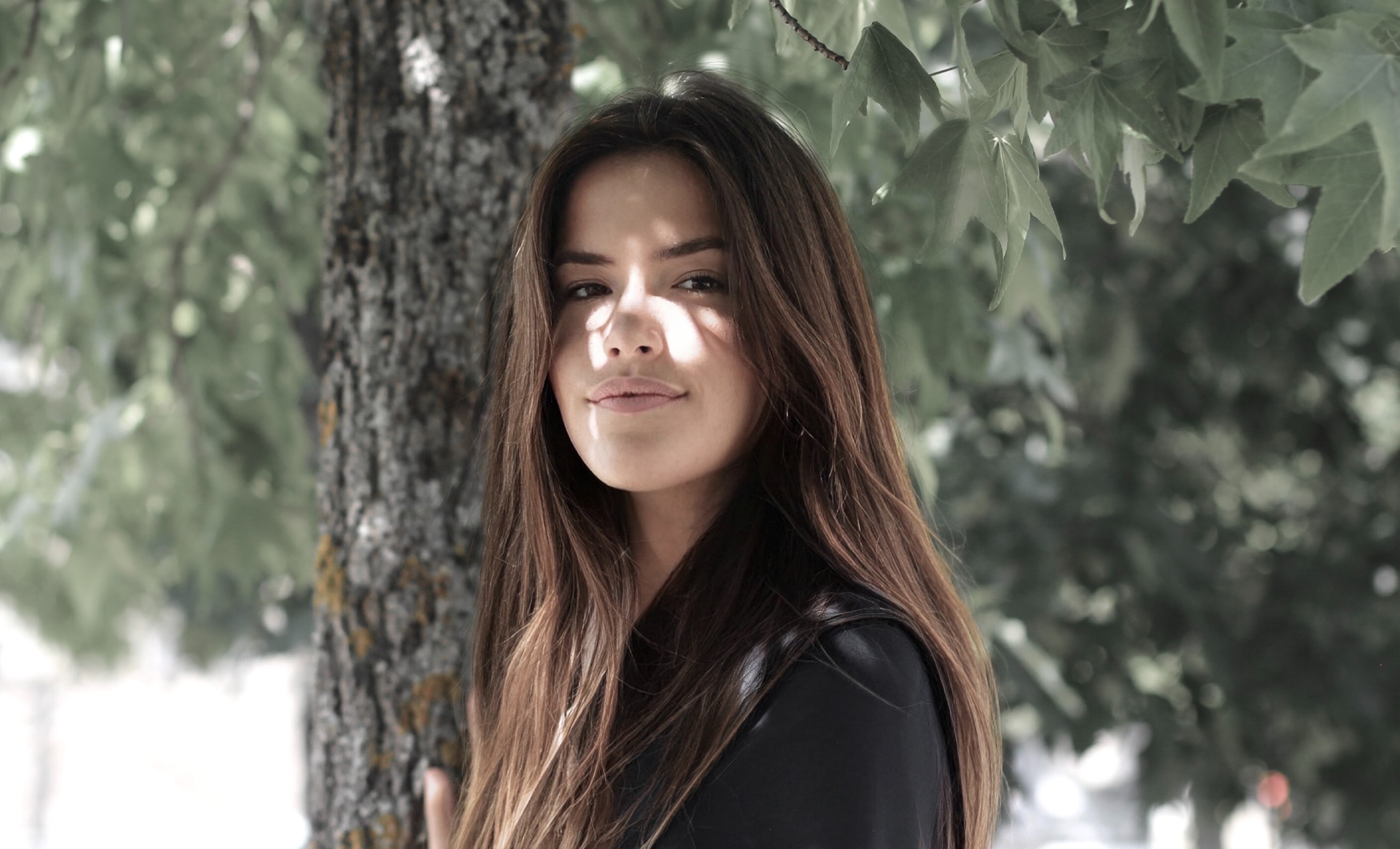 Portrait d'une jeune femme brune souriante sous les feuillages